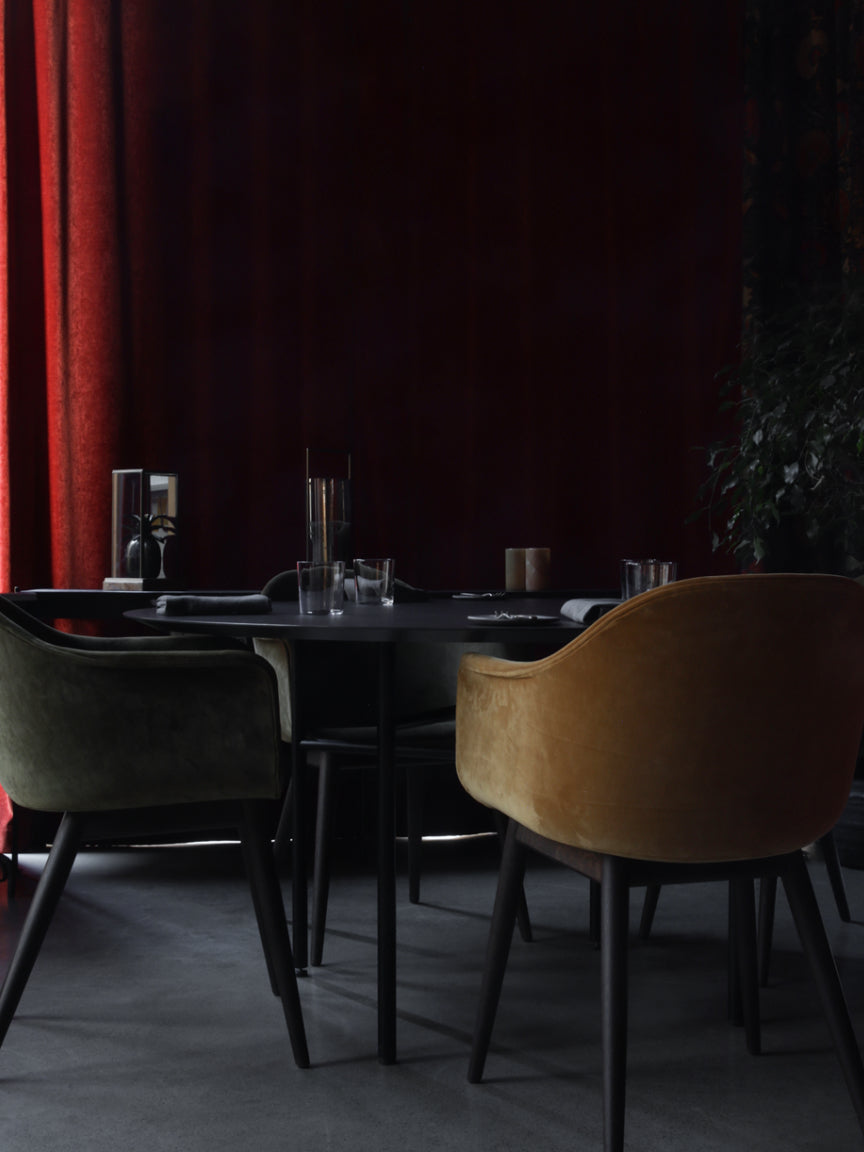 Dining area with dark table and chairs against a red curtain.