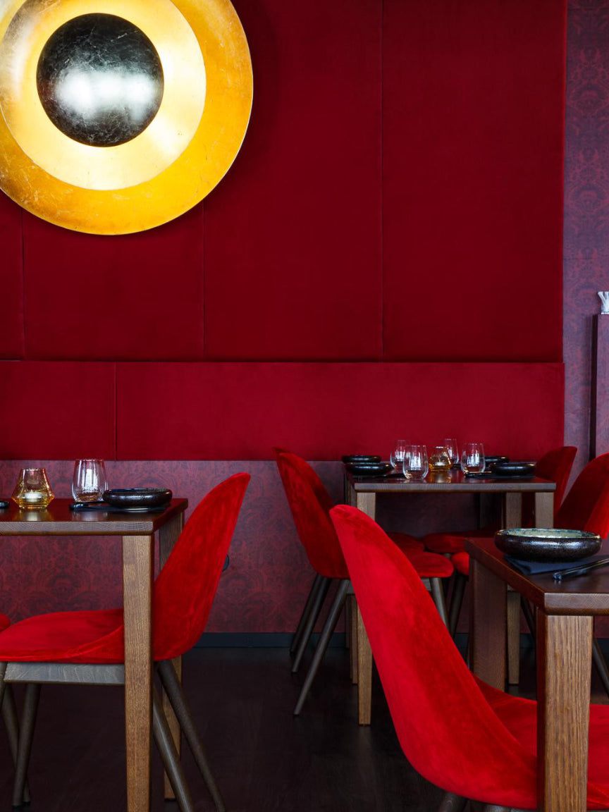 Dining area with red chairs and a red wall, featuring a round yellow light fixture.
