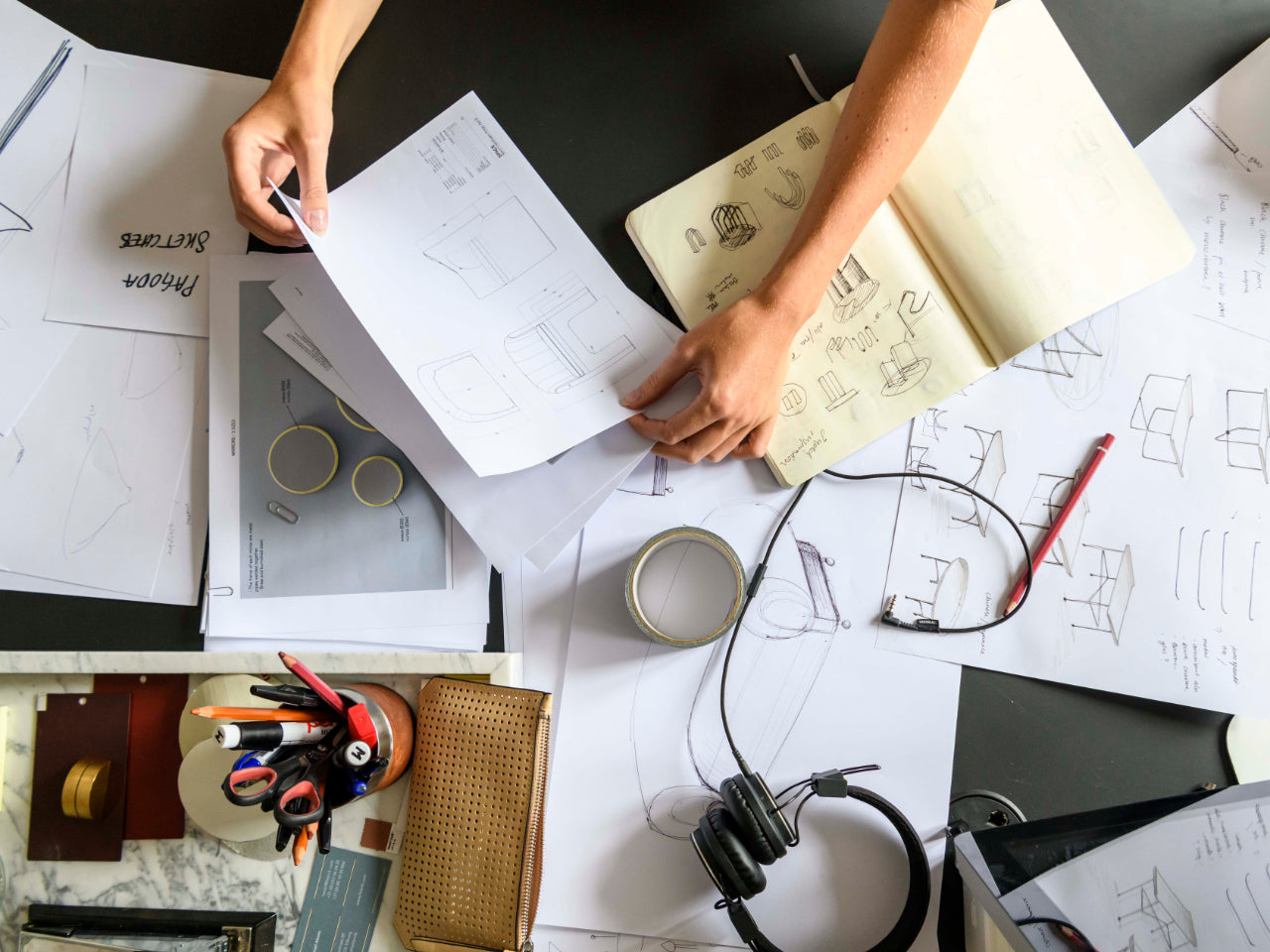 Person working at a desk with architectural drawings, notes, and office supplies.