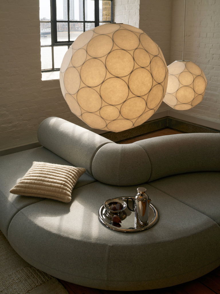 Round gray sofa with a decorative lamp and small table in a room with large windows. 