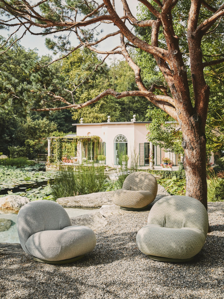 Three modern outdoor chairs under a tree with a house and garden in the background