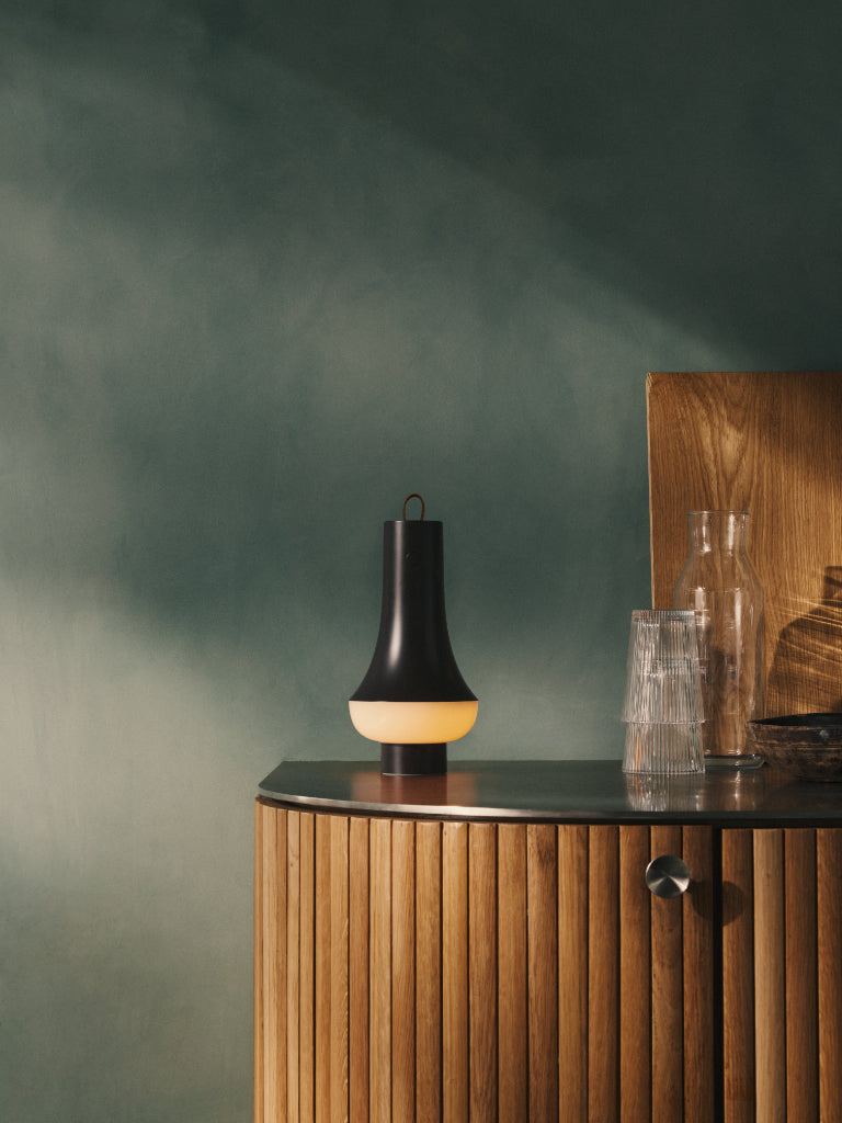 Modern black and beige lamp on a wooden sideboard against a green wall