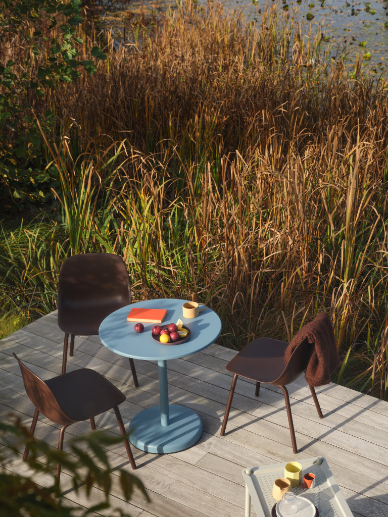 Outdoor setting with a round blue table and chairs near tall grasses.