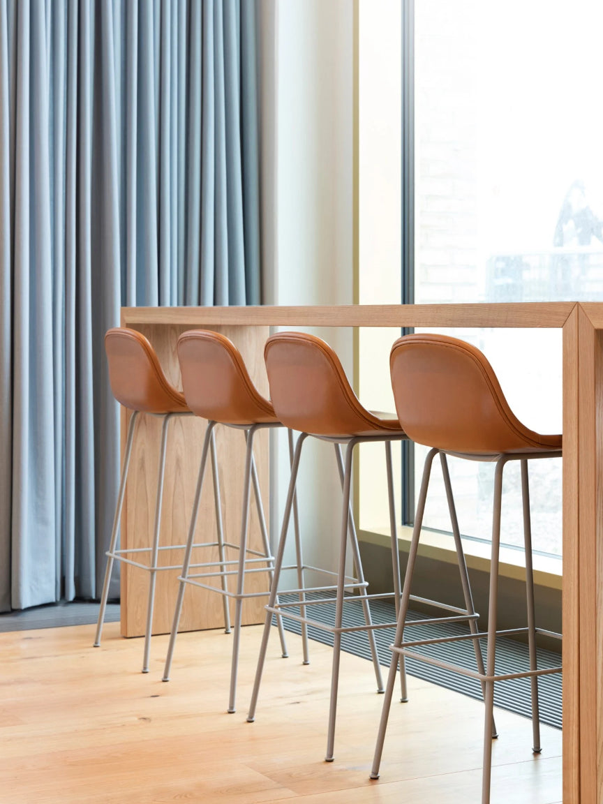 Four brown bar stools with metal legs in front of a window with light blue curtains.