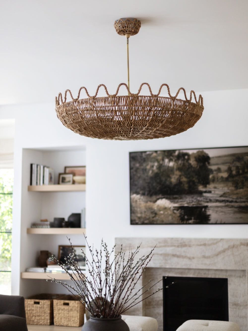A large woven wicker chandelier with a scalloped edge hangs in a bright, modern living room above a fireplace.