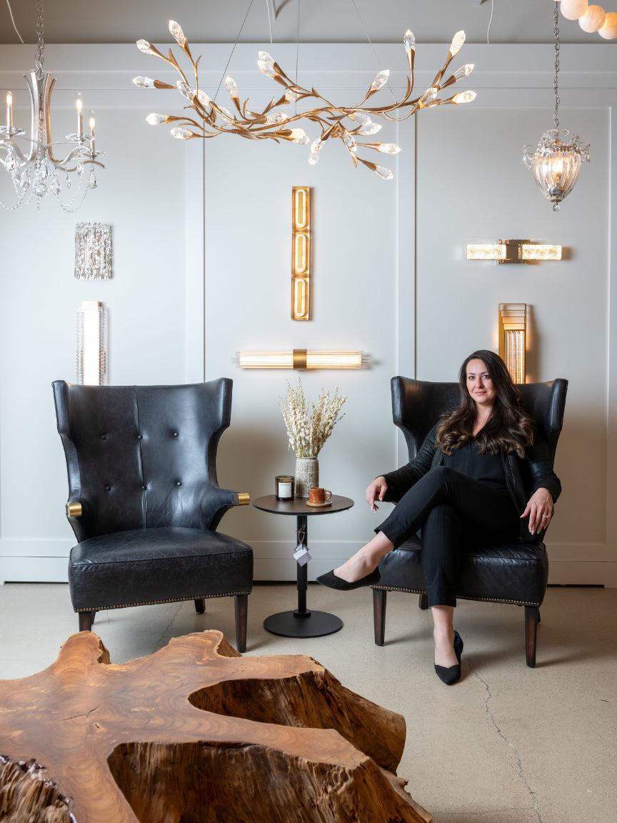 Woman sitting in a stylish room with modern decor, including black leather chairs and a wooden table.