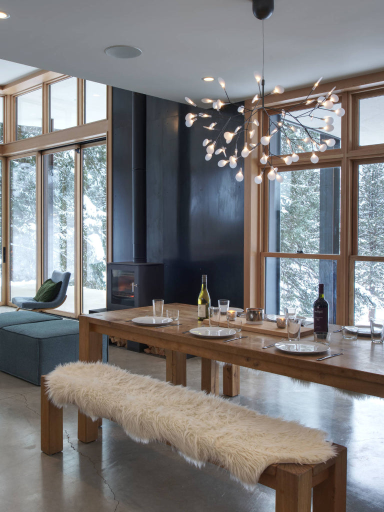 Moooi chandelier in modern dining room with wooden table, bench, and large windows.