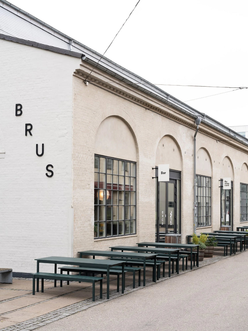 Outdoor seating area with green tables and benches in front of a building with 'BRUS' branding.