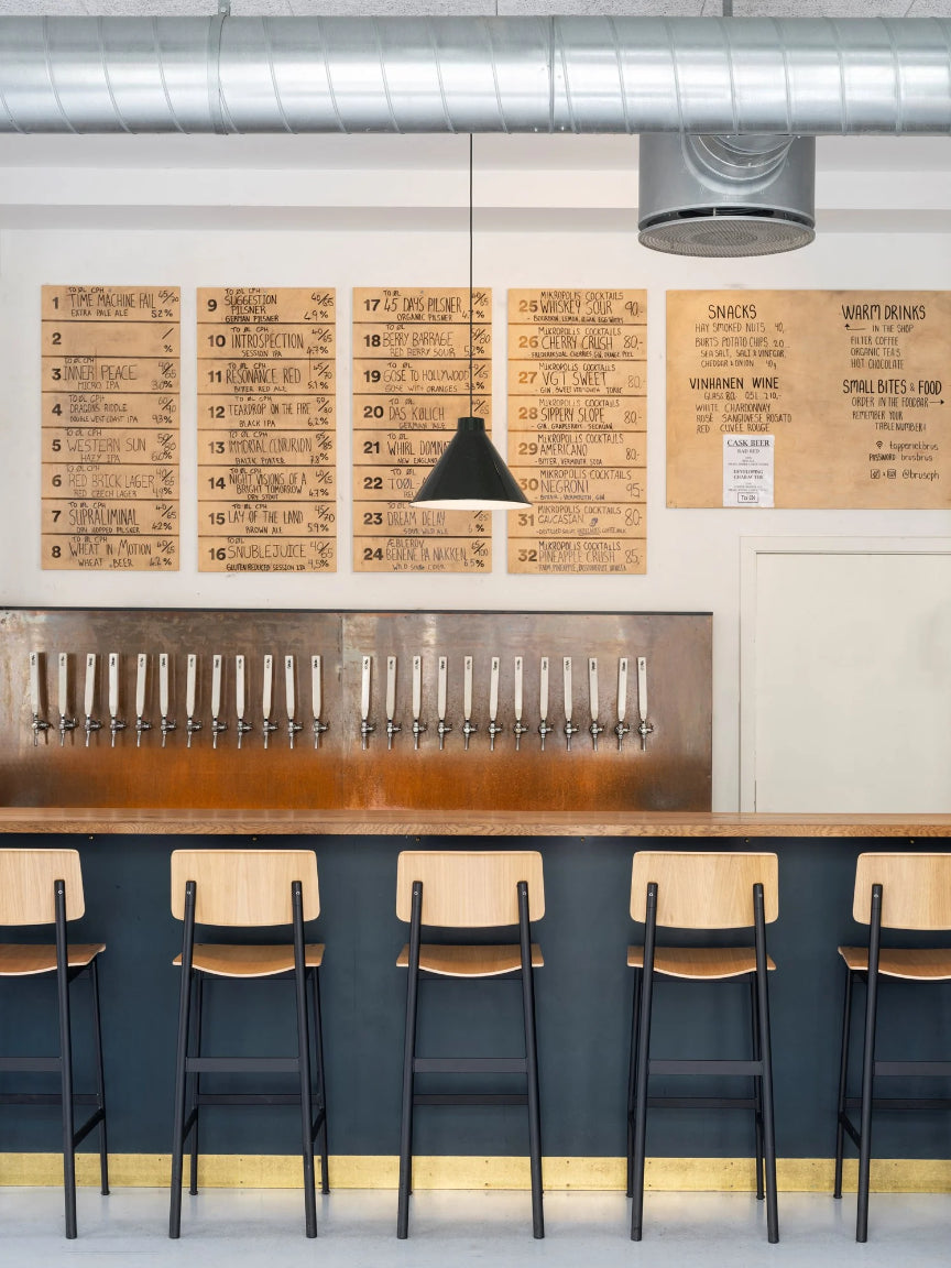 Bar setup with wooden stools and a wall of beer taps in a modern interior.