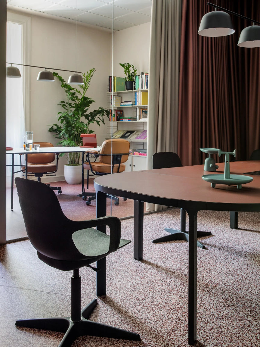 Modern office space with round tables and chairs, plants, and a bookshelf.