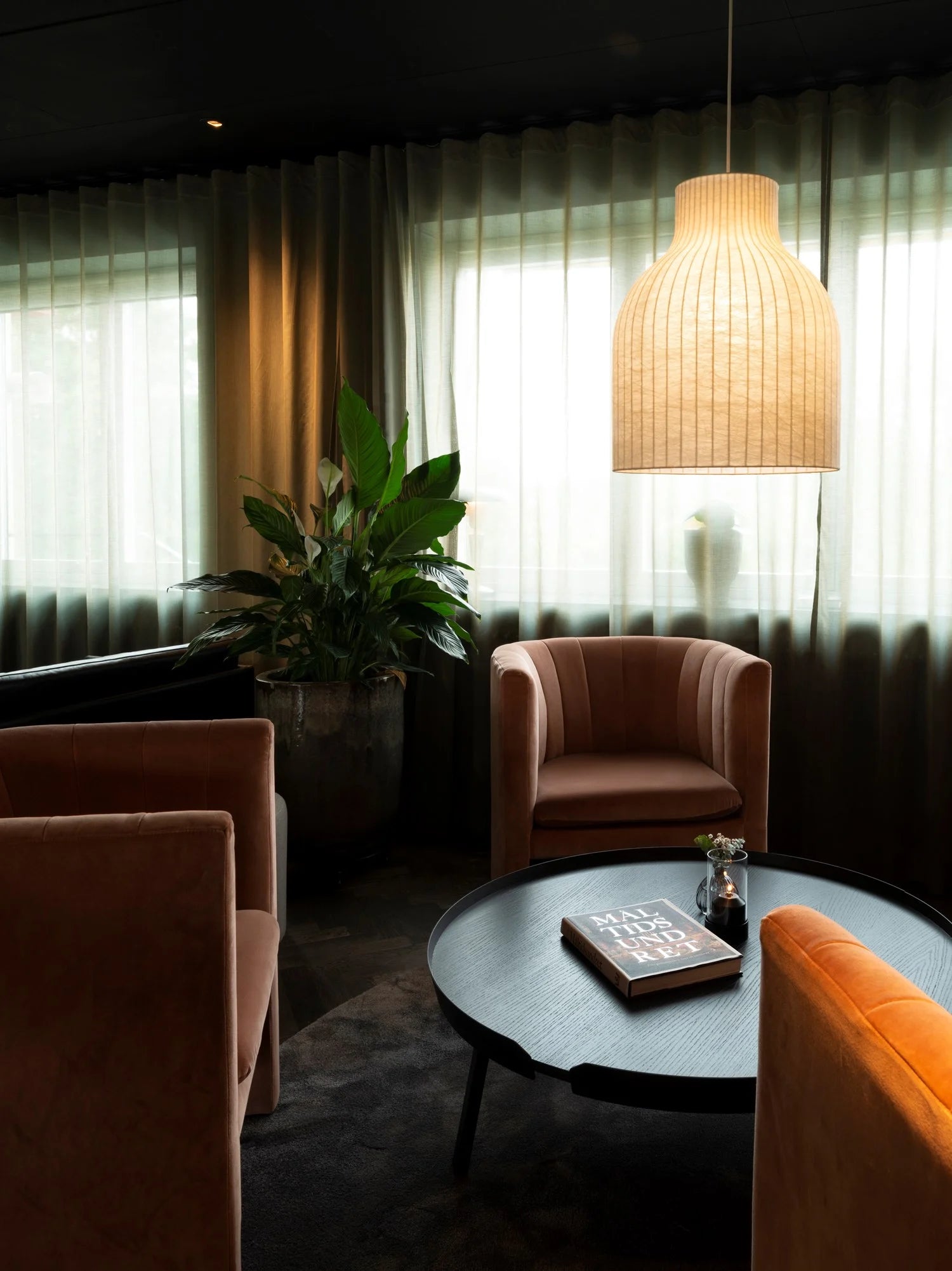 Modern living room with pink armchairs, a round coffee table, and a hanging light fixture.