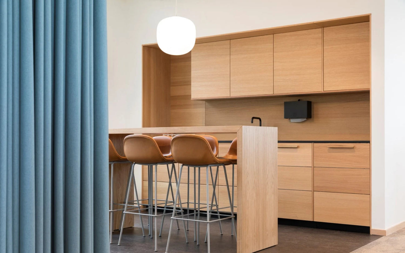Modern kitchen with wooden cabinets, bar stools, and a blue curtain.