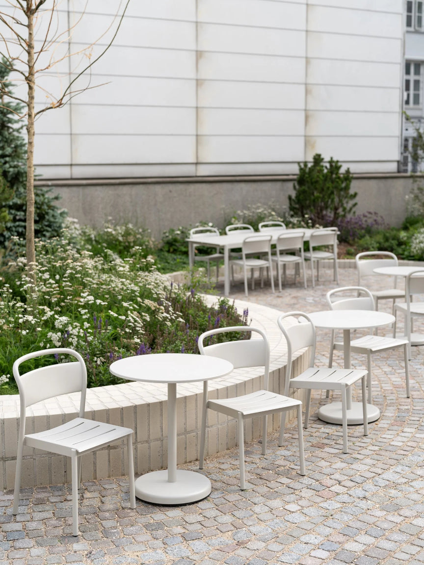 Outdoor seating area with white tables and chairs in a garden setting.
