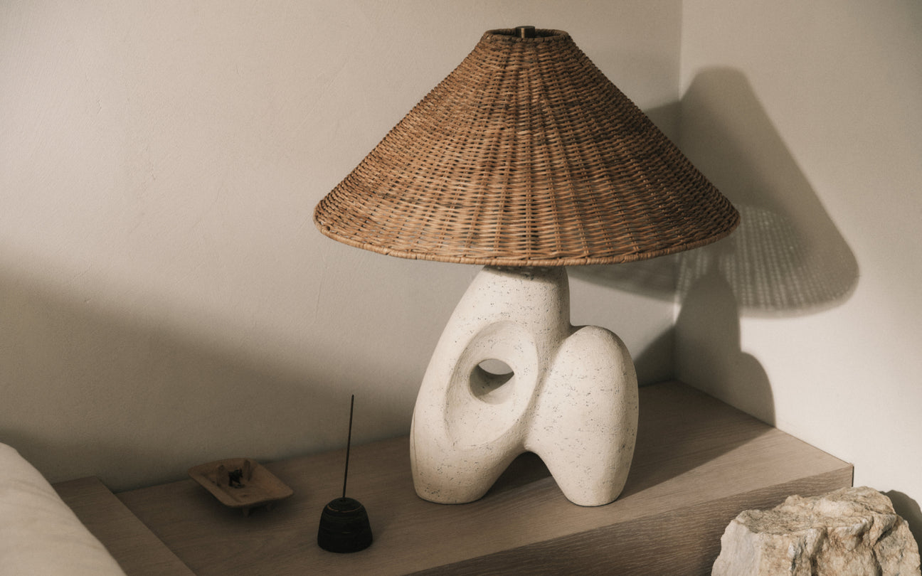 Table lamp with wicker shade and stone base on a shelf against a neutral wall.