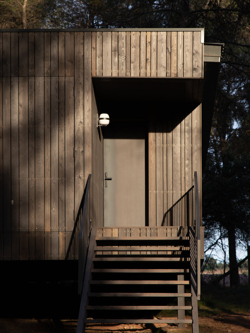 Wooden cabin with steps leading up to a door, surrounded by trees