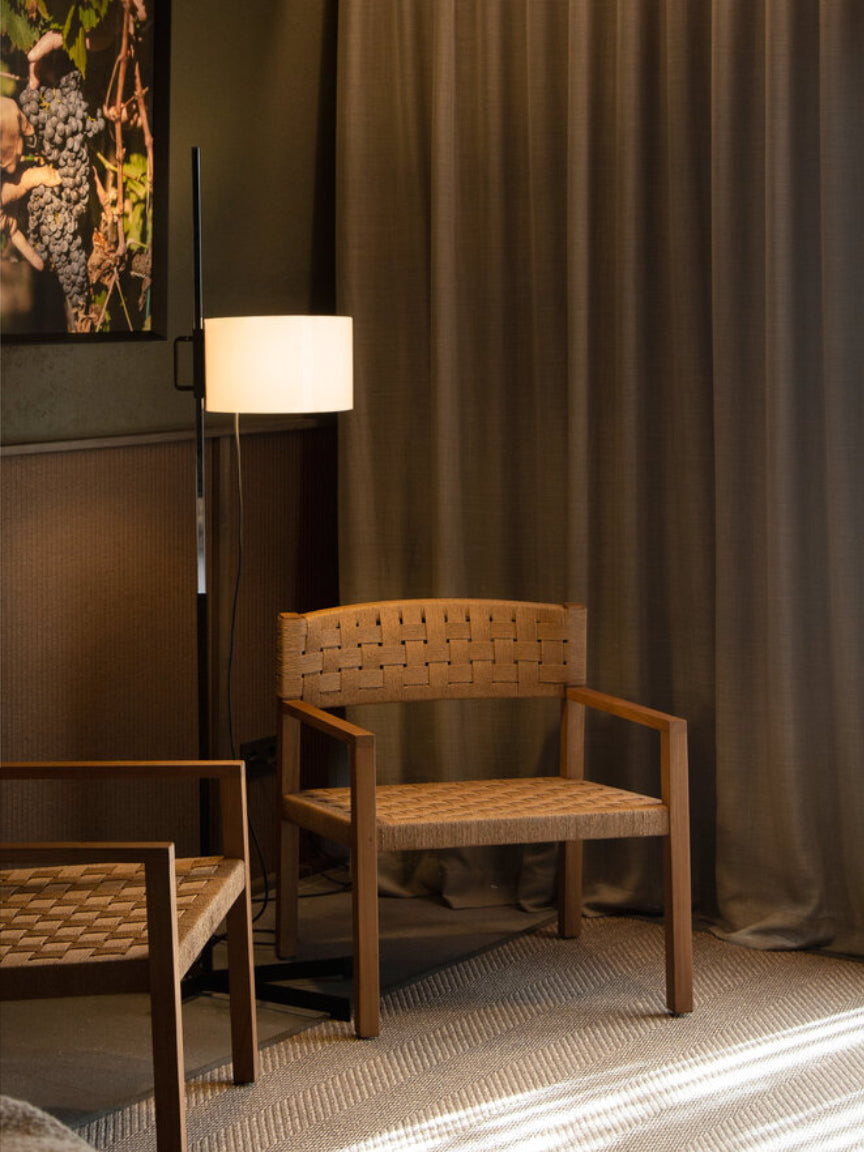 Wooden chair with woven seat and backrest in a room with a lamp and curtains.