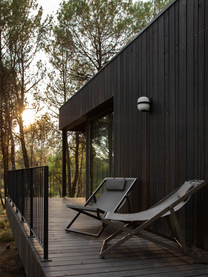 Modern house exterior with lounge chairs on a wooden deck during sunset.