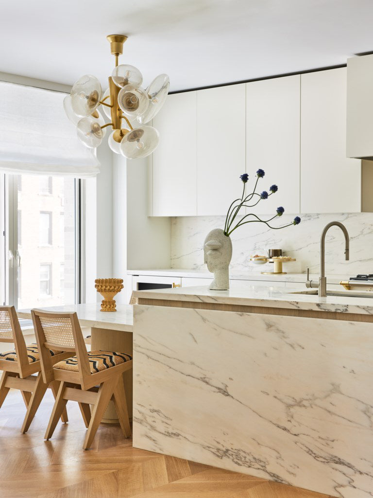 Modern kitchen with marble island, wooden chairs, and decorative elements.