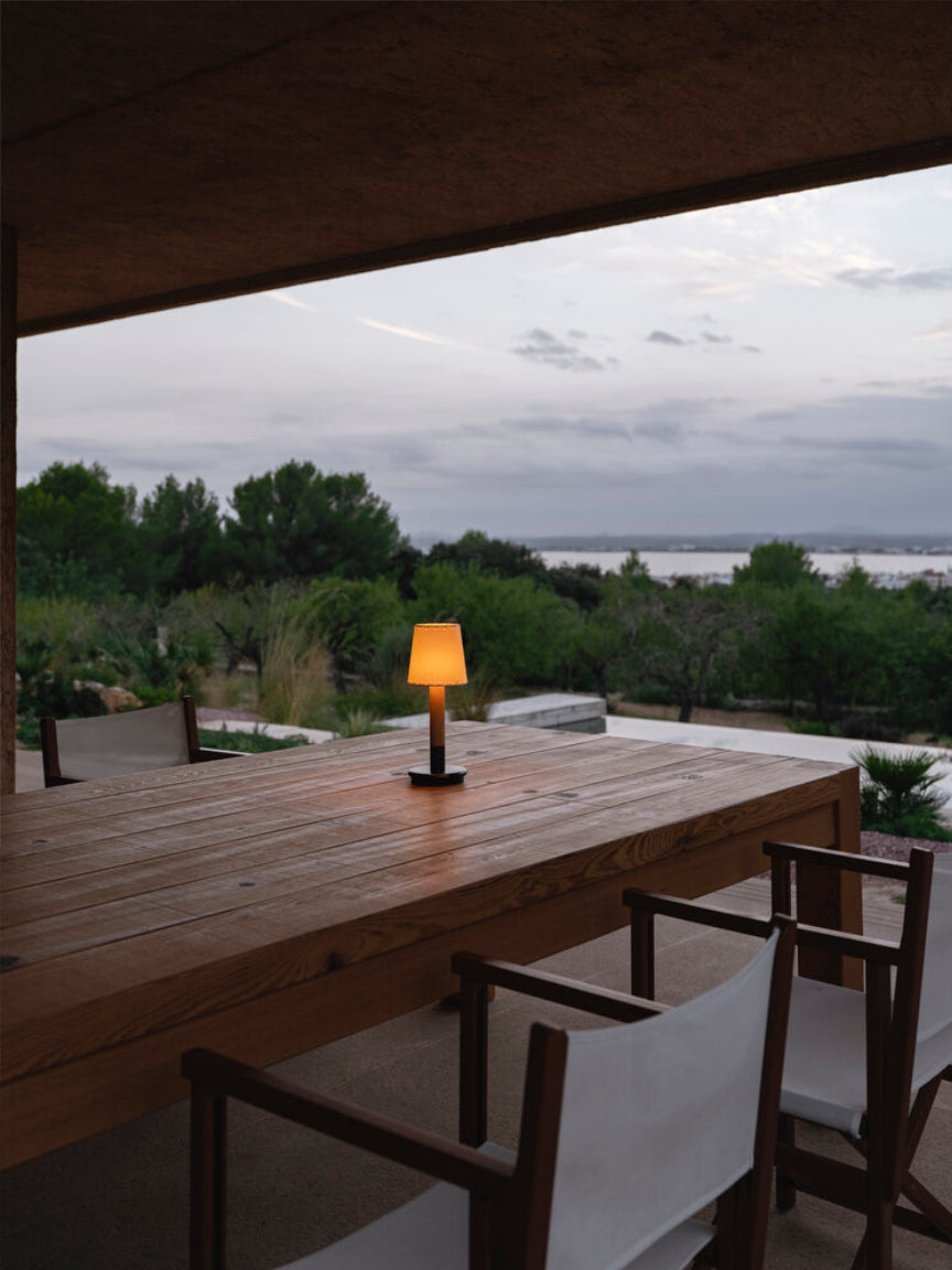 Outdoor wooden table with a lamp and chairs, overlooking a scenic view.