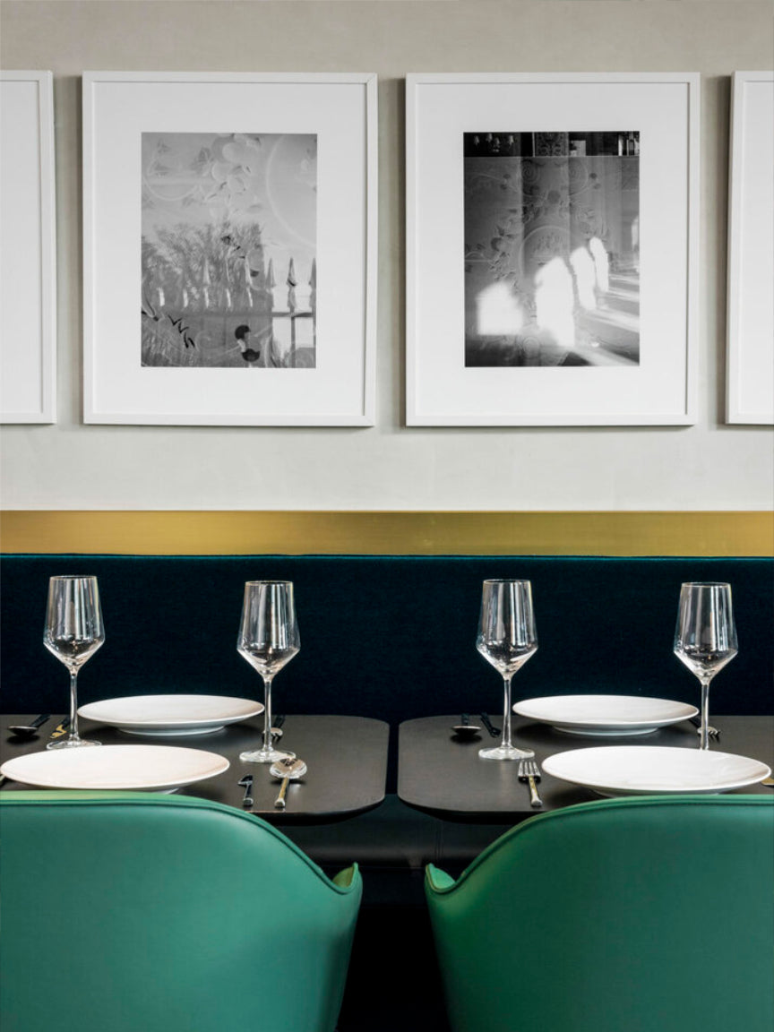 Dining area with green chairs, black table, wine glasses, plates, and framed art on the wall.