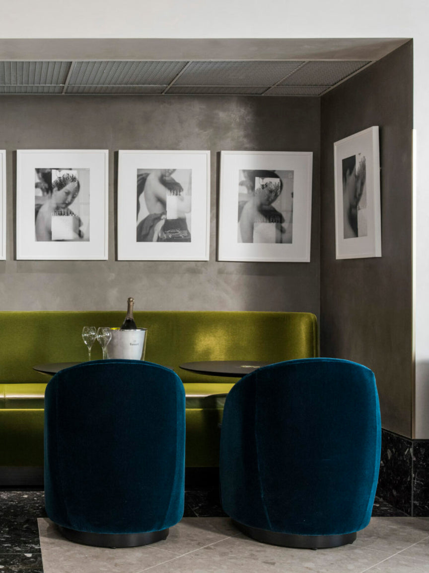 Two blue chairs in a modern interior setting with a green booth and framed pictures on the wall.