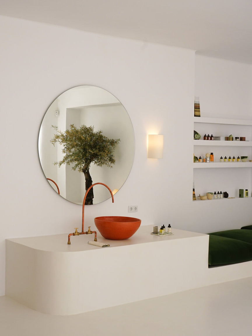 Modern bathroom with round mirror, copper faucet, and orange sink.