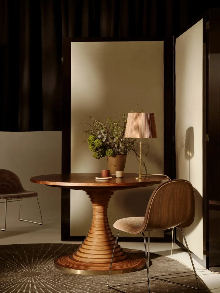 Wooden dining table with chairs in a dimly lit room. Tavolo a dischi table by Gubi.